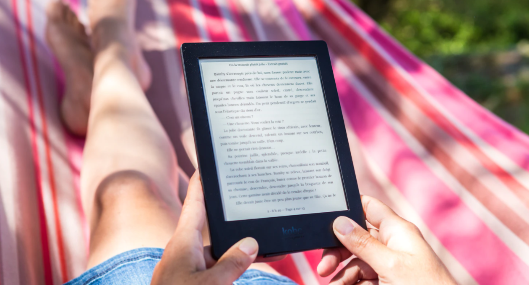 Lady sat on a pink stripy hammock reading a book on a tablet.