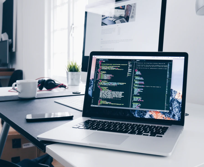 Code displayed on a laptop, on a desk with a computer in the background. 